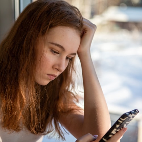 Worried teen girl reading threatening message on mobile phone